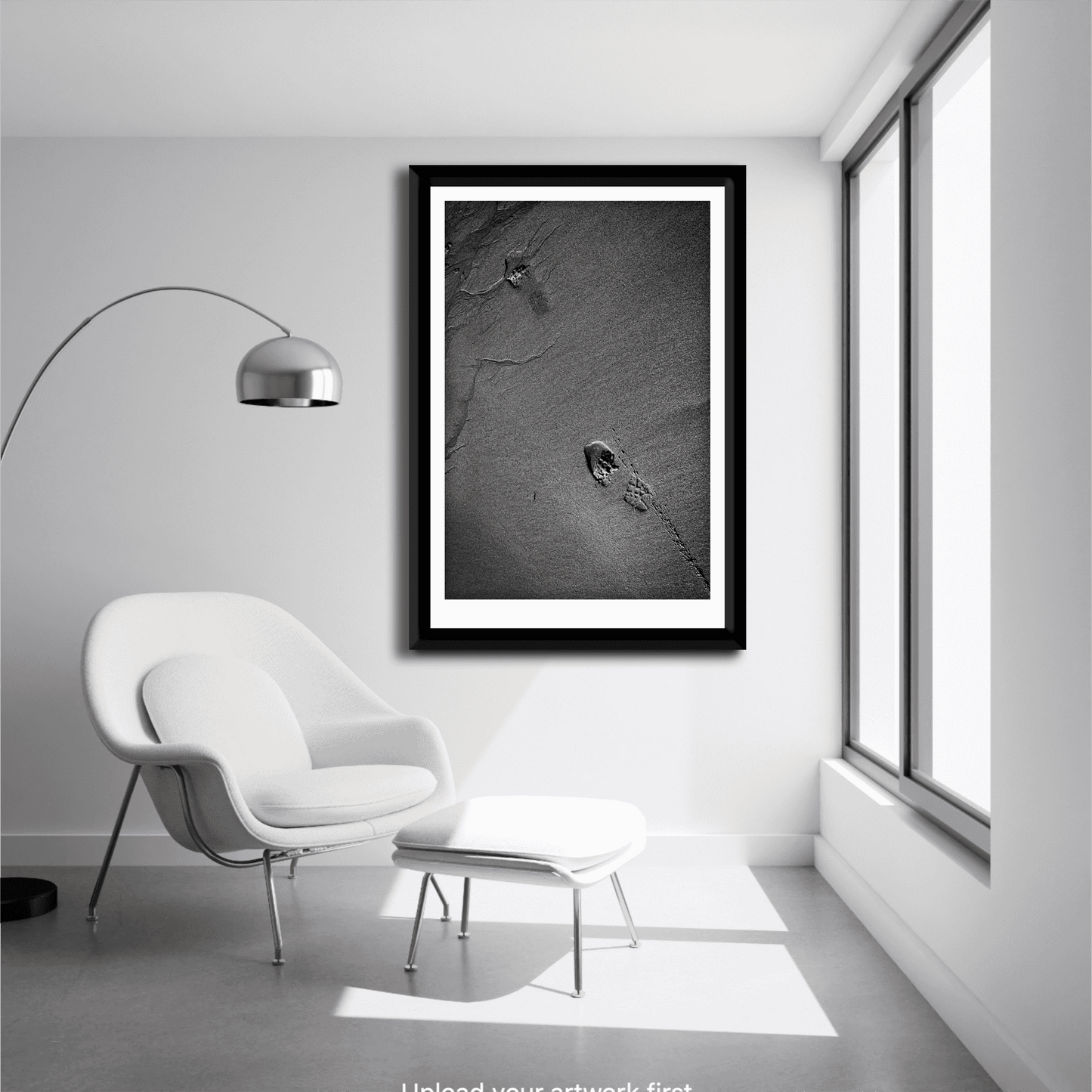 Minimalist room with lounge chair featuring framed Traces #1 – black and white sand and footprint fine art print in vertical composition.