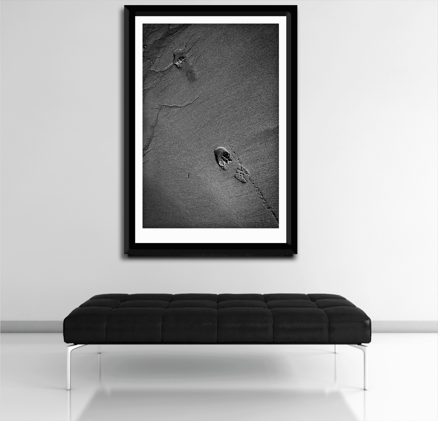 Modern black and white interior with framed Traces #1 sand and footprint fine art photo above a sleek bench, ideal for contemporary decor.