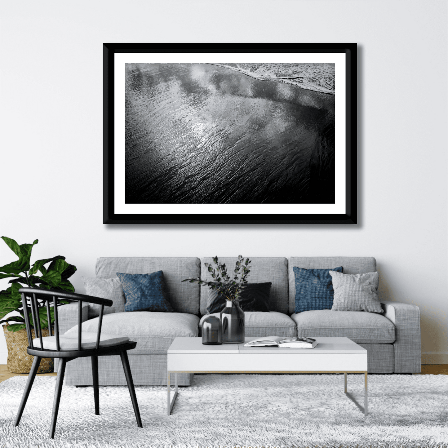 Modern living room with framed 'Traces #4 – Reflections at the Sea Edge, Maine' black and white ocean reflection print above gray sofa and coffee table.