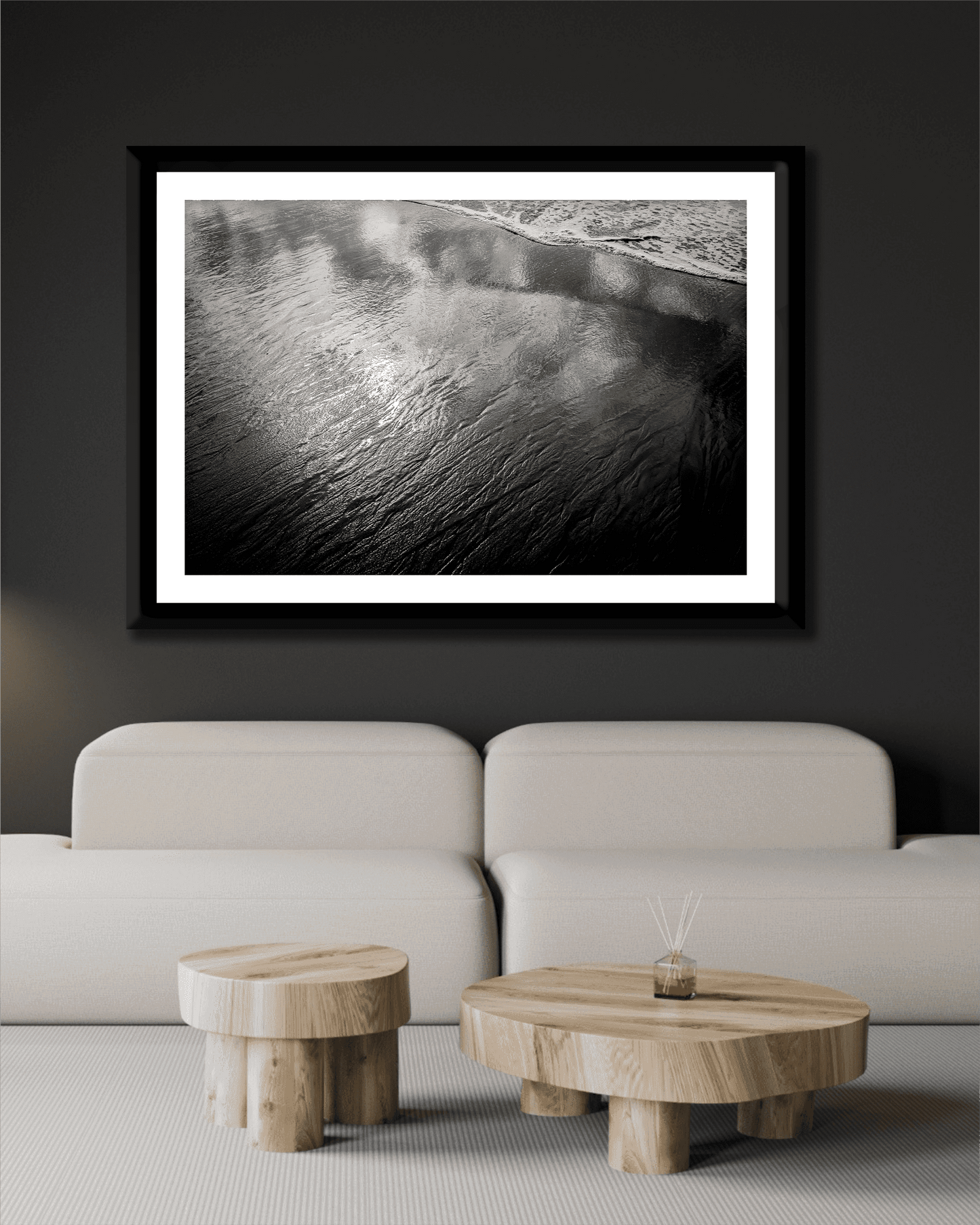 Contemporary black wall decor with framed 'Traces #4 – Reflections at the Sea Edge, Maine' above cream sofa and wooden coffee tables in minimalist style.