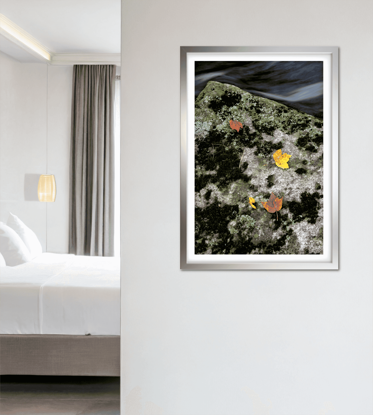 Autumn Remains – Limited Edition Photograph framed in white, hanging in a minimalist bedroom, showcasing golden leaves on mossy rock for serene decor.