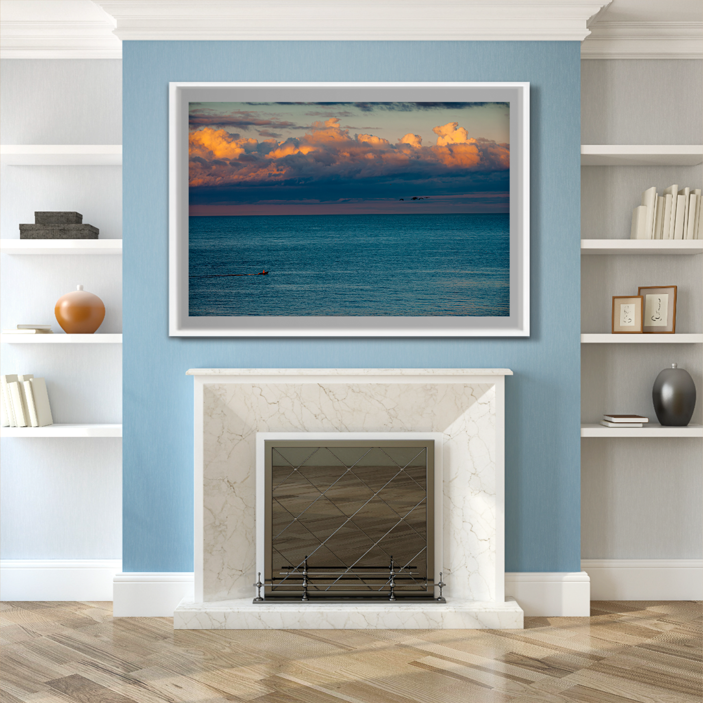 The Race – Small Boat and Birds in a New England Coastal Sunset framed artwork mounted above a fireplace in a blue and white traditional living room.