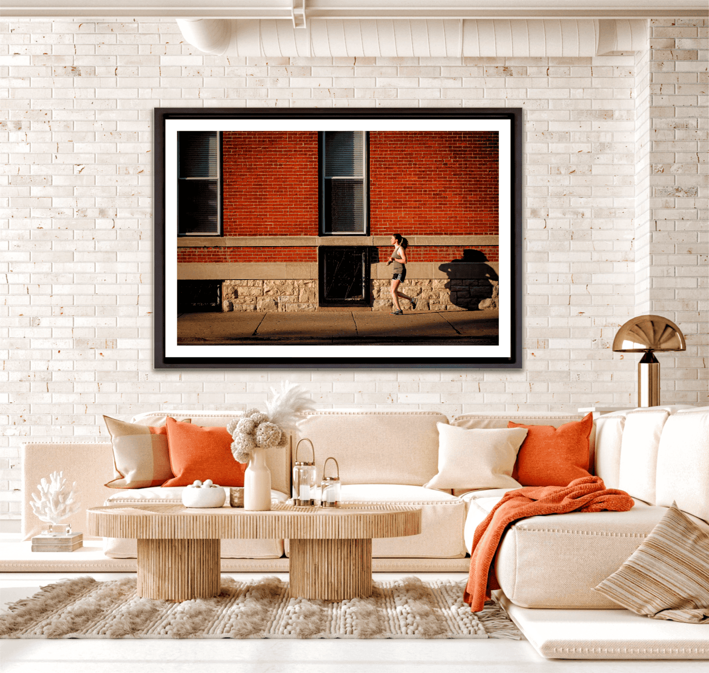 Framed print in a rooms setting of woman jogging along a sidewalk in Chicago, in the early evening summer light, against. red brick facade.