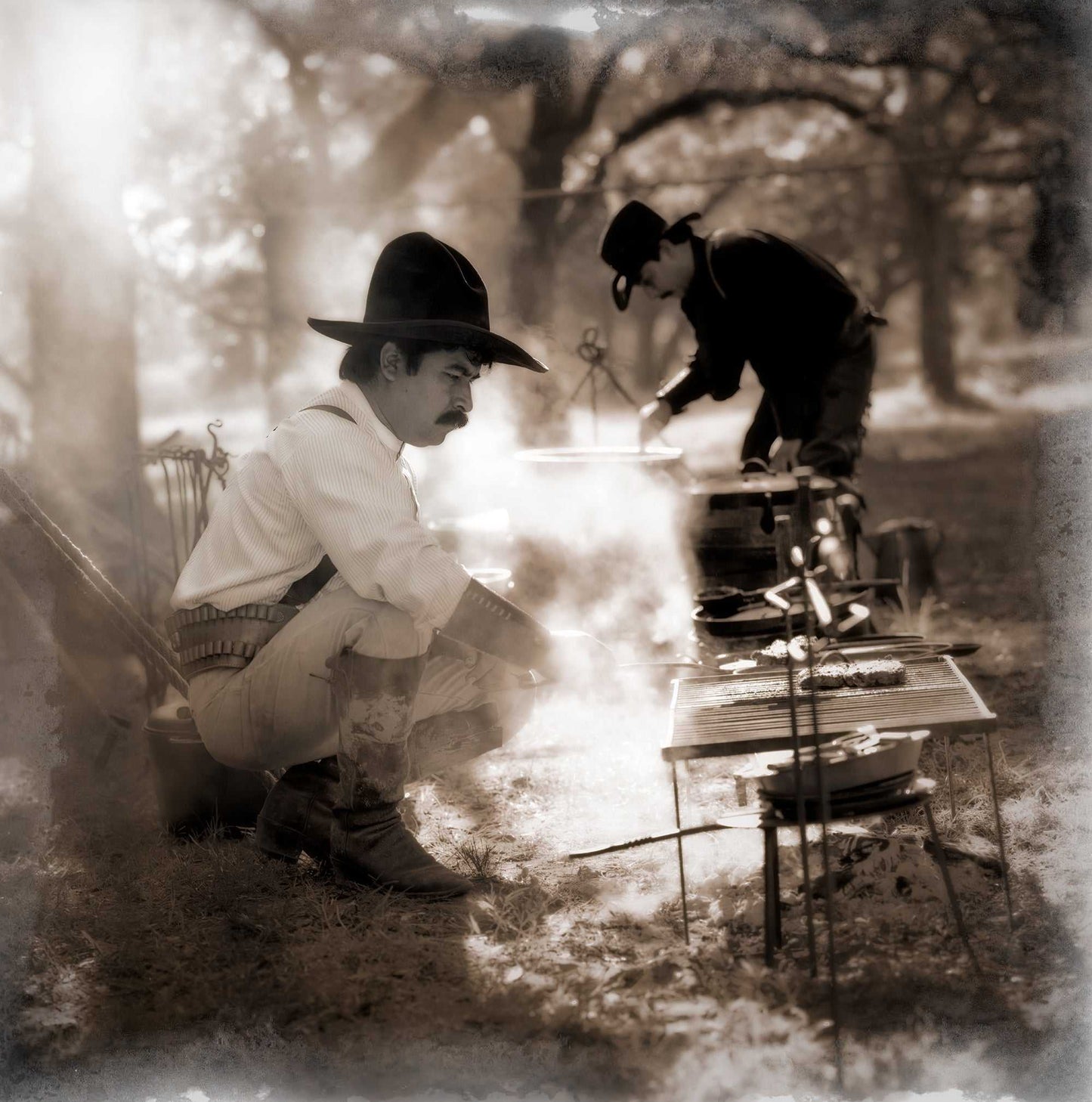 Sepia-toned Hasselblad film photo of two cowboys cooking at a chuckwagon campfire, showcasing authentic Western heritage and cast iron cookware.