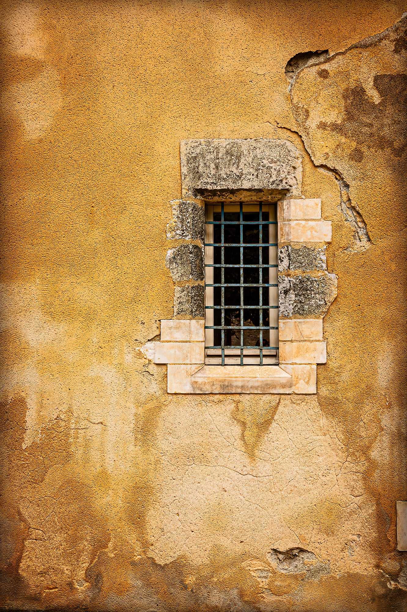 Golden Wall – Aged Texture and Light in Historic Troyes, France featuring a weathered yellow stucco wall with a barred stone window. Fine art print for rustic European interior decor.