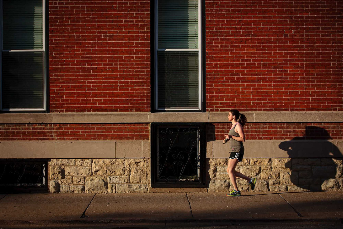 Photo of woman jogging along a sidewalk in Chicago, in the early evening summer light, against. red brick facade.