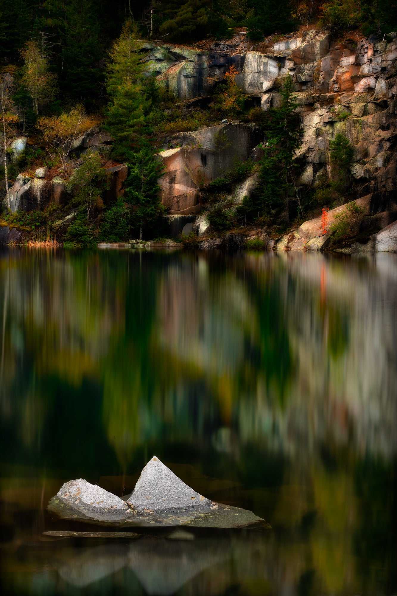 The Sentinel – A Lone Rock Emerges Above The Quarry Waterline, Maine features a jagged rock in still water with autumn forest reflections and quarry cliffs.
