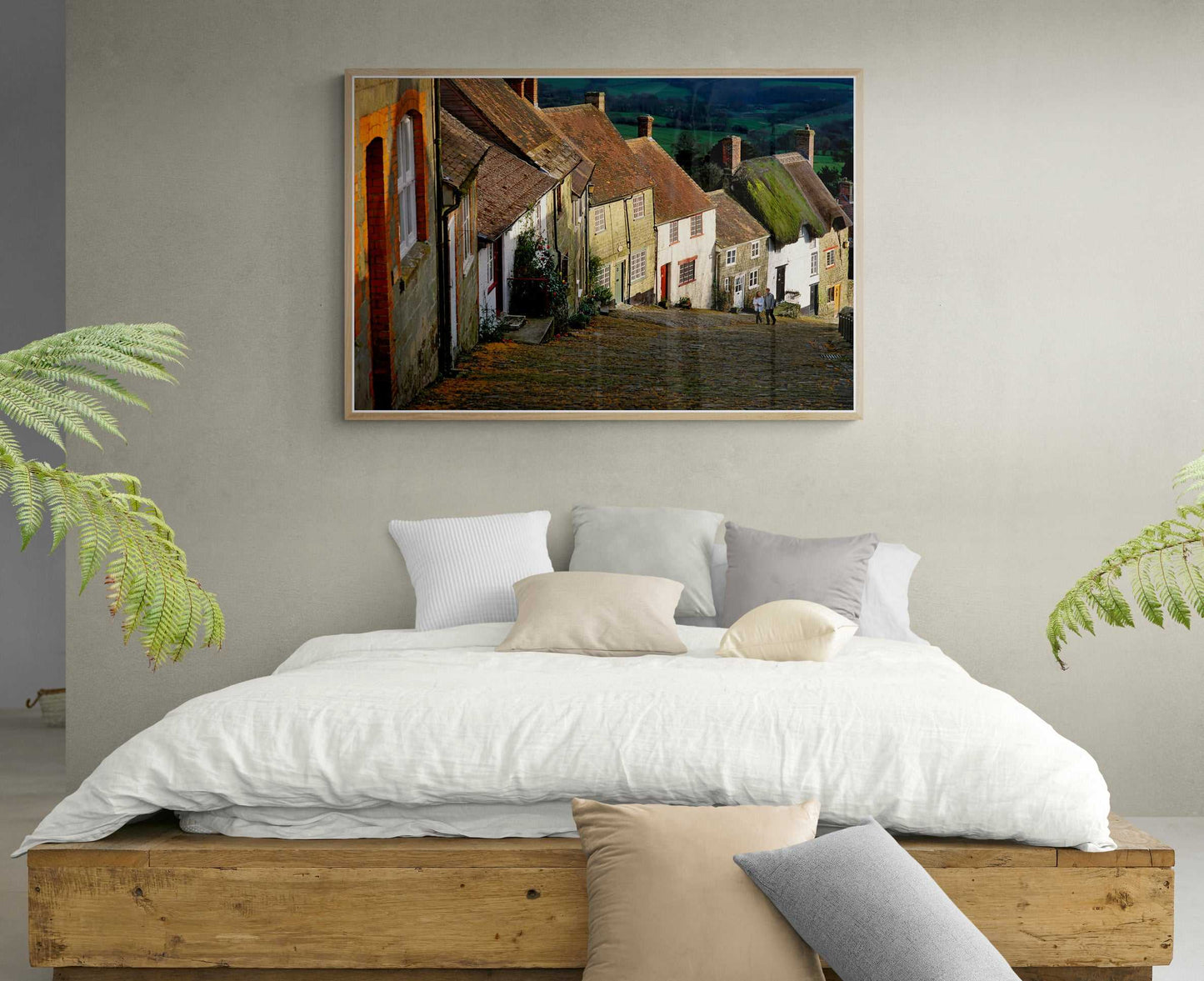 Gold Hill, Shaftesbury – A Fairy Tale Scene in Dorset wall art above a rustic bed in a cozy bedroom with neutral tones and indoor plants.