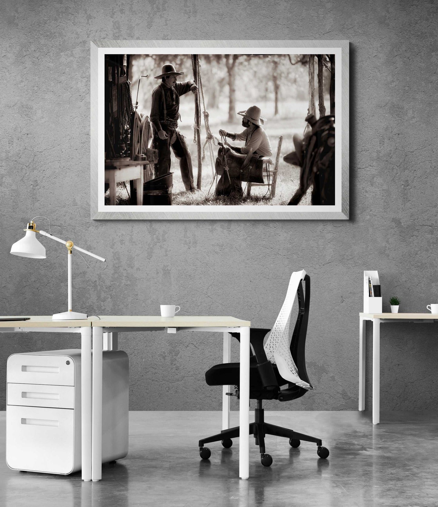 Limited edition Old West photography print 'Camp Talk: A Chuckwagon Cook-Off in Authentic Old West Style' framed in white and featured in a modern office with dual desks and white decor.