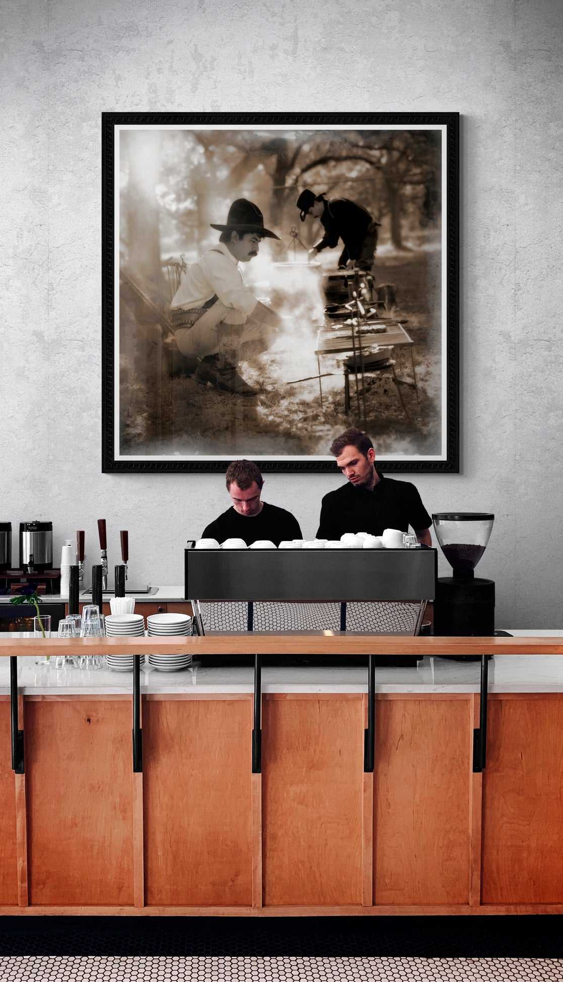 Chuckwagon photography print of cowboys cooking over fire, featured in modern café interior, merging Western lifestyle art with urban decor.