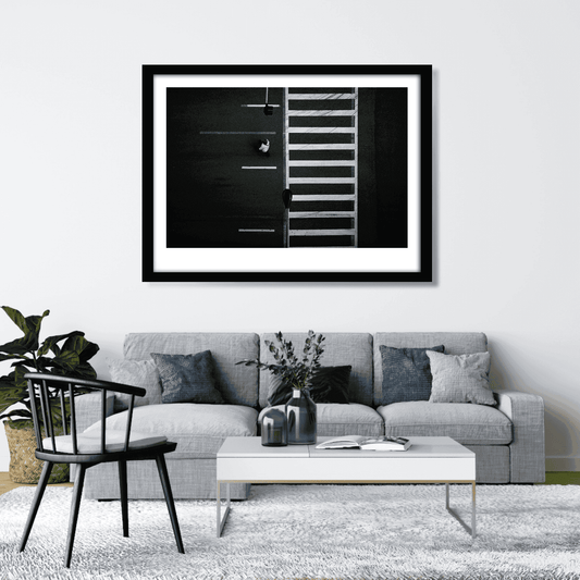 Framed overhead black and white photograph of Chicago crosswalk with pedestrian and graphic street pattern shown oin a clean neutral living room.