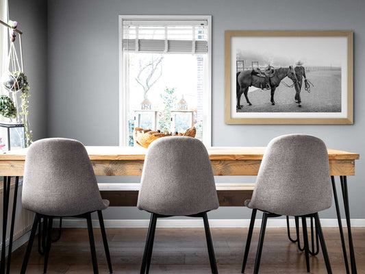 Morning Ride – Saddling Up in the Fog, Black and White Ranch Print by Michael Hart displayed in a modern dining room with gray walls and wooden table. Limited edition Texas ranch wall art featuring cowboy life and horses in a misty landscape.