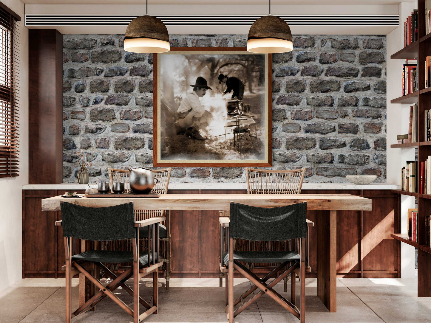 Framed Western heritage art print of chuckwagon cooking scene displayed in rustic dining room with stone wall, ideal for ranch-style home decor.