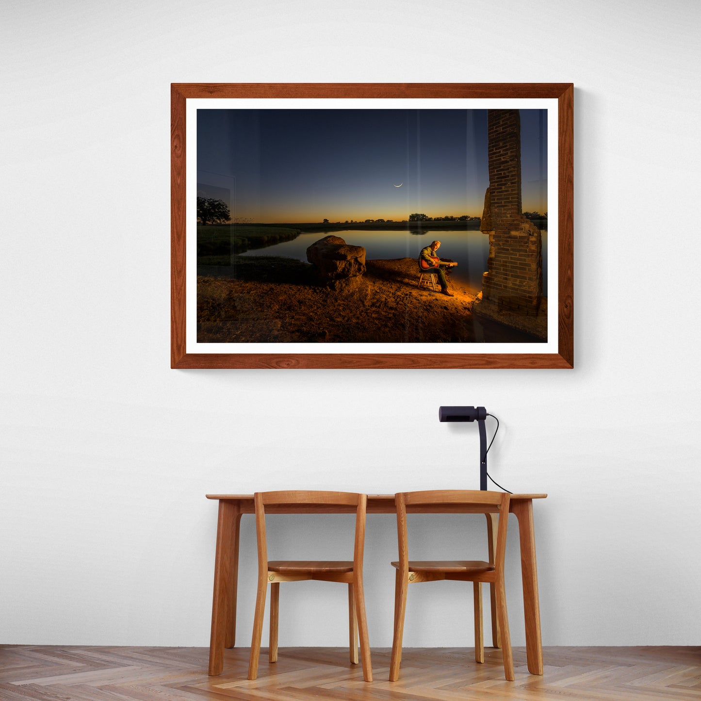 Framed photograph of a Texas singer-songwriter in front of a chimney by a tank at sunset on a wall above a wooden table and chairs.