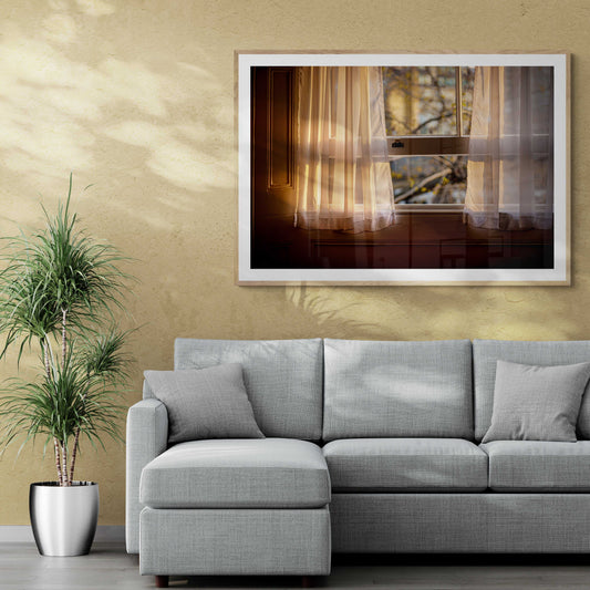 Framed wall art 'From A Window: Golden Light on Lace Curtains in a London Hotel Room' displayed above a modern gray sectional in a stylish living room.