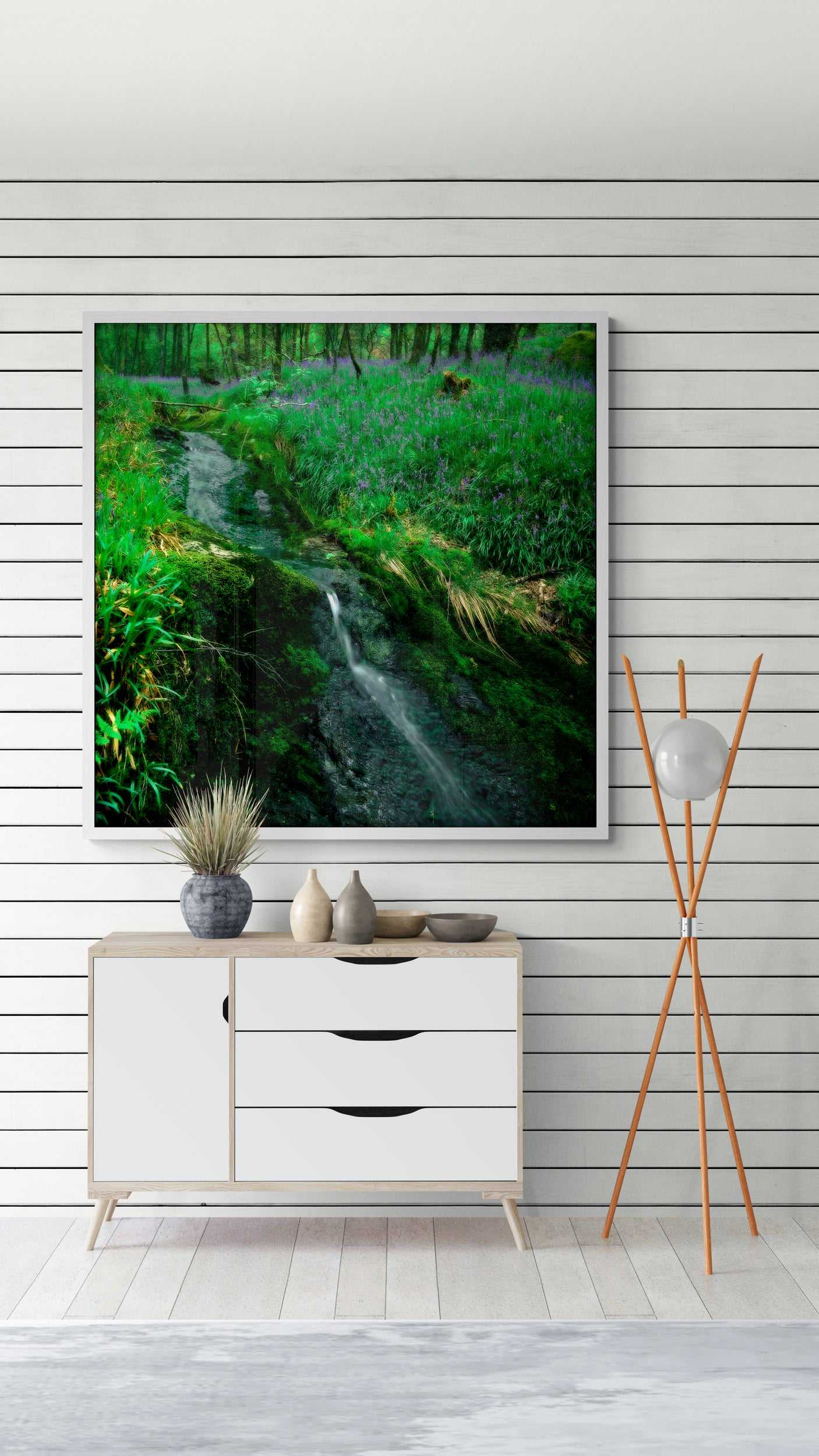 Framed Lomond Creek fine art Scotland print displayed in a modern white living room, showcasing a lush creek and wildflower glen near Loch Lomond.