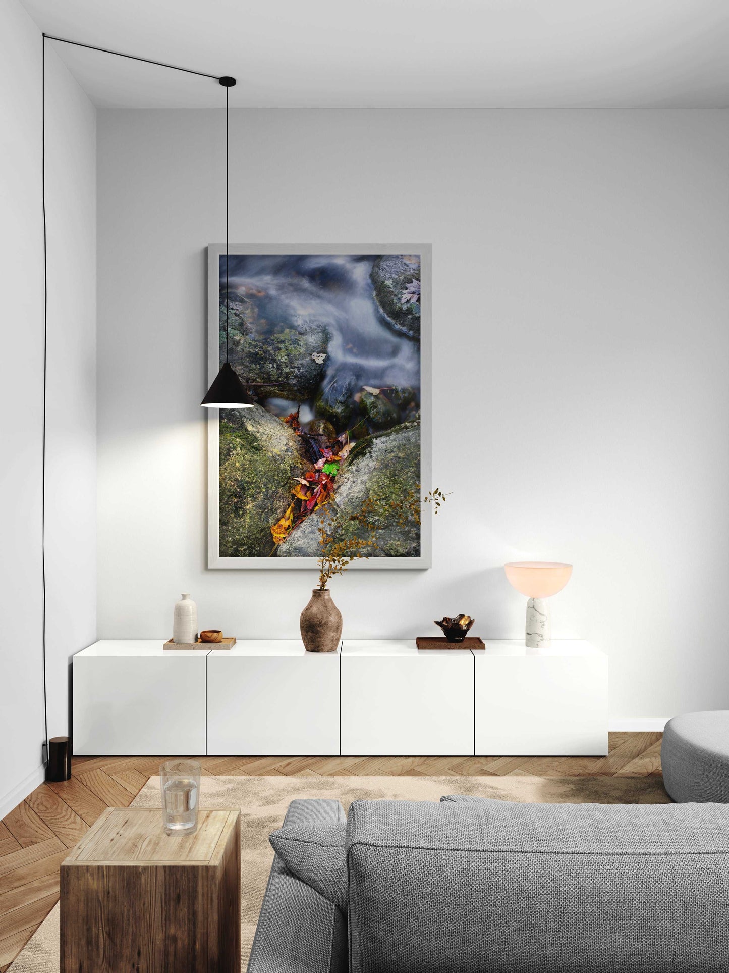 Vertical framed First Frost photograph of a Maine stream with fall leaves, styled in a minimalist white living room with modern furniture and lighting.