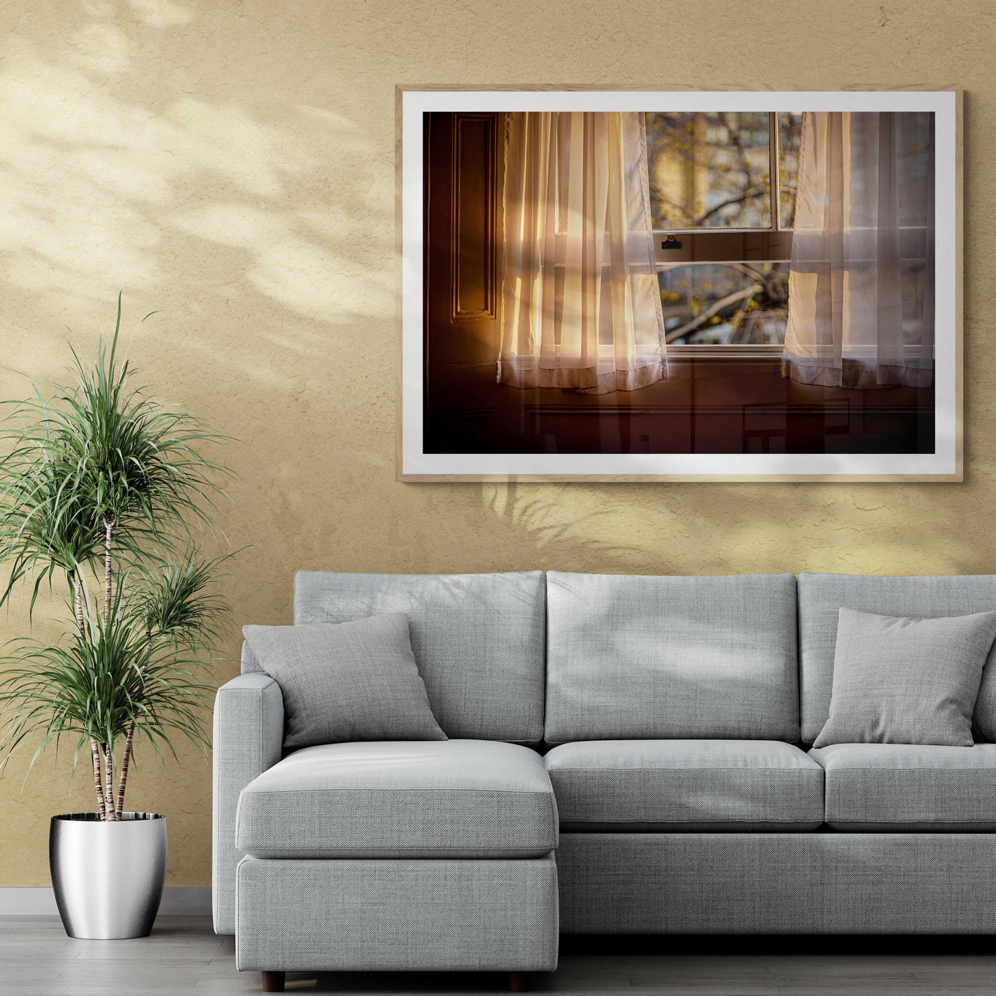 Framed wall art 'From A Window: Golden Light on Lace Curtains in a London Hotel Room' displayed above a modern gray sectional in a stylish living room.