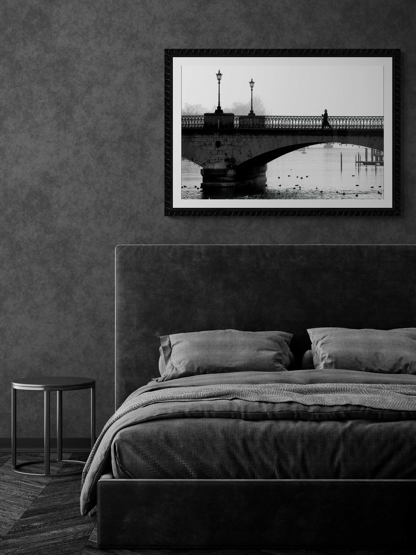 Zurich Series #1 – A Man on the Bridge, Zurich in Black and White – Fine Art Print by Michael Hart mounted above a grey upholstered bed in a dark-toned minimalist bedroom.