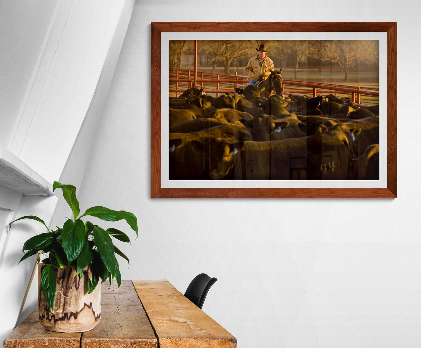 Morning Roundup at 44 Farms cowboy and Angus cattle print by Michael Hart displayed above a wooden desk in a cozy, plant-accented workspace.