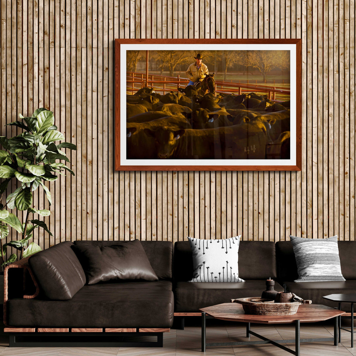 Rustic-themed living room with wood paneling featuring Morning Roundup at 44 Farms cowboy and cattle fine art print by Michael Hart in a brown frame.