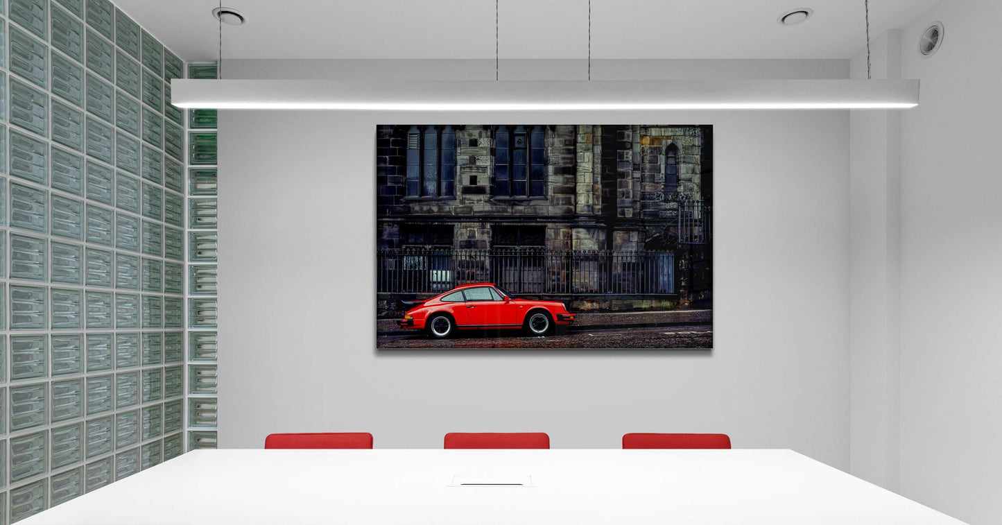 Automotive fine art print of red Porsche and historic cathedral, featured in a sleek office meeting room with red chairs.