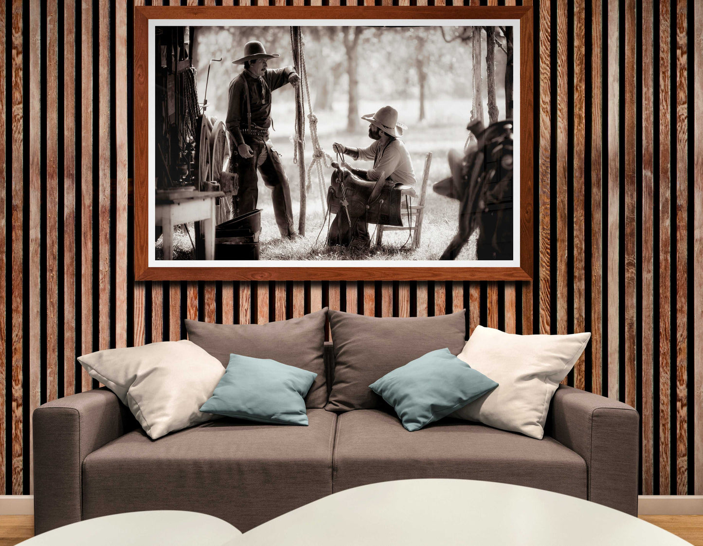 Framed Western lifestyle art print 'Camp Talk: A Chuckwagon Cook-Off in Authentic Old West Style' displayed above a modern gray sofa with accent pillows, blending rustic charm with contemporary decor.
