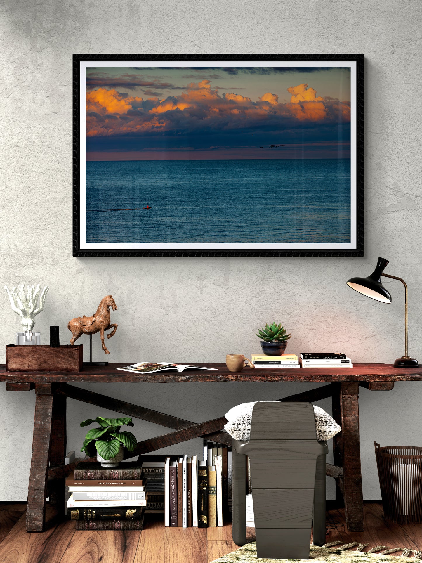 Framed print of The Race – Small Boat and Birds in a New England Coastal Sunset displayed above a rustic desk, ideal for coastal-themed interior design.