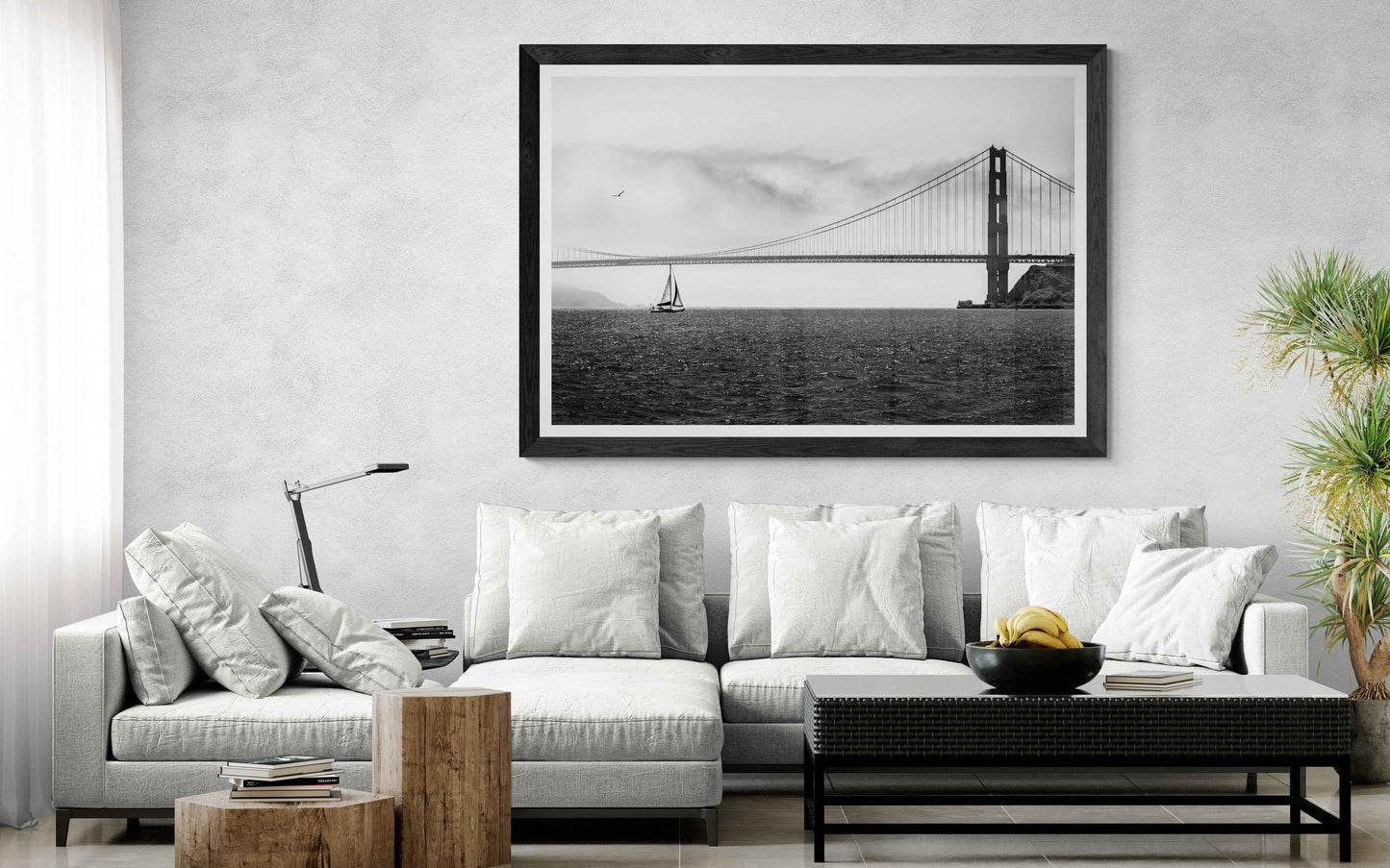Large framed black and white print of a sailboat under The Golden Gate Bridge on the wall of a modern, highly living room