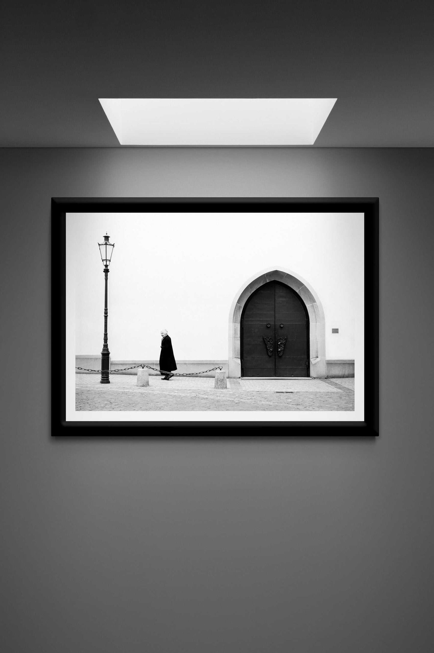 Zurich Series #2 – The Woman and the Church, Black and White Fine Art Print by Michael Hart displayed under a skylight in a sleek, monochrome-themed gallery space.