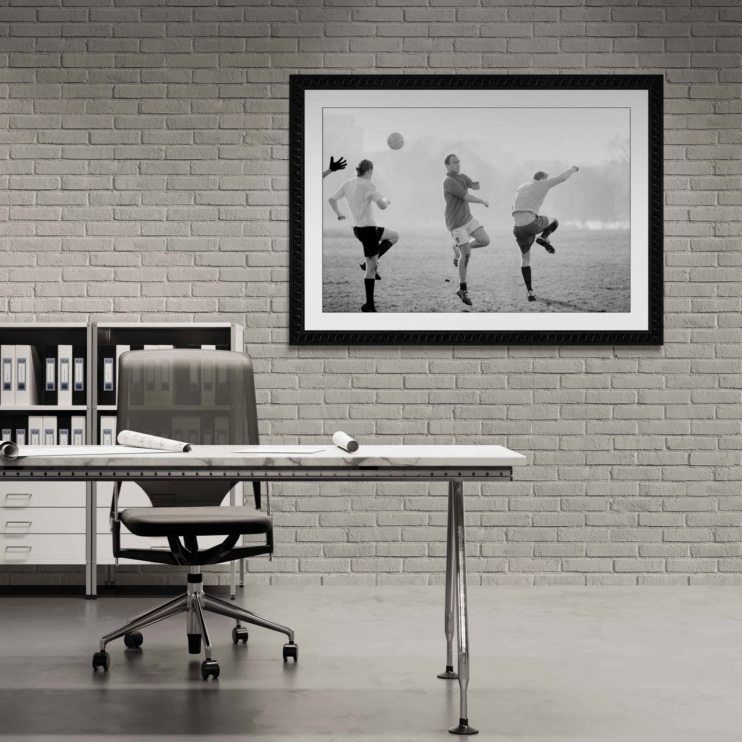 Framed black and white print of soccer players framed on abrick wall in a minimalist office setting.