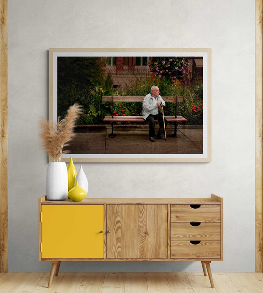 Troyes France Art Print features an elderly man seated on a bench in a lush French garden, capturing a quiet street moment. Limited edition fine art for home decor.