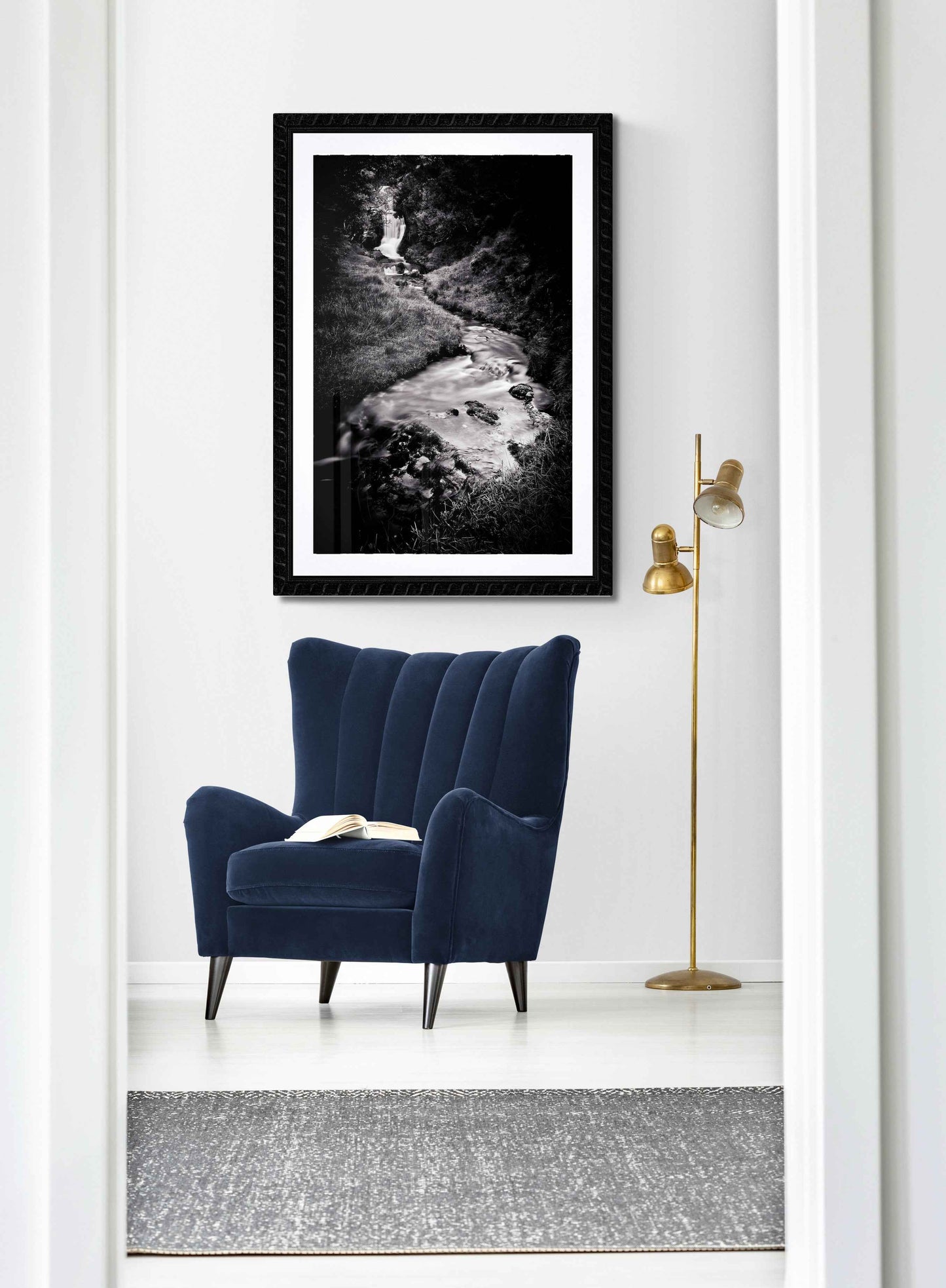 Silk and Stone, Sutherland framed waterfall print in a cozy reading nook with navy chair and gold lamp, perfect for elegant home decor.