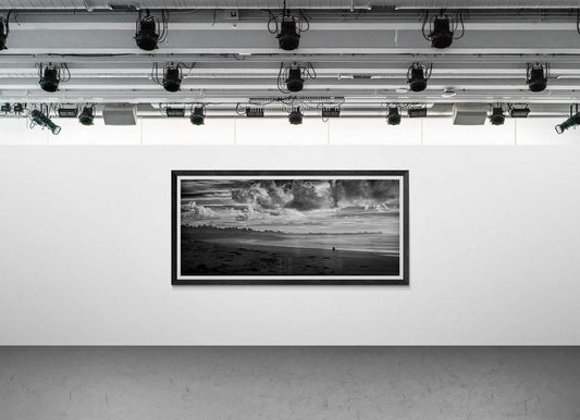 Framed black and white panoramic photograph of a person and dog on Monterey Bay displayed on a modern gallery wall