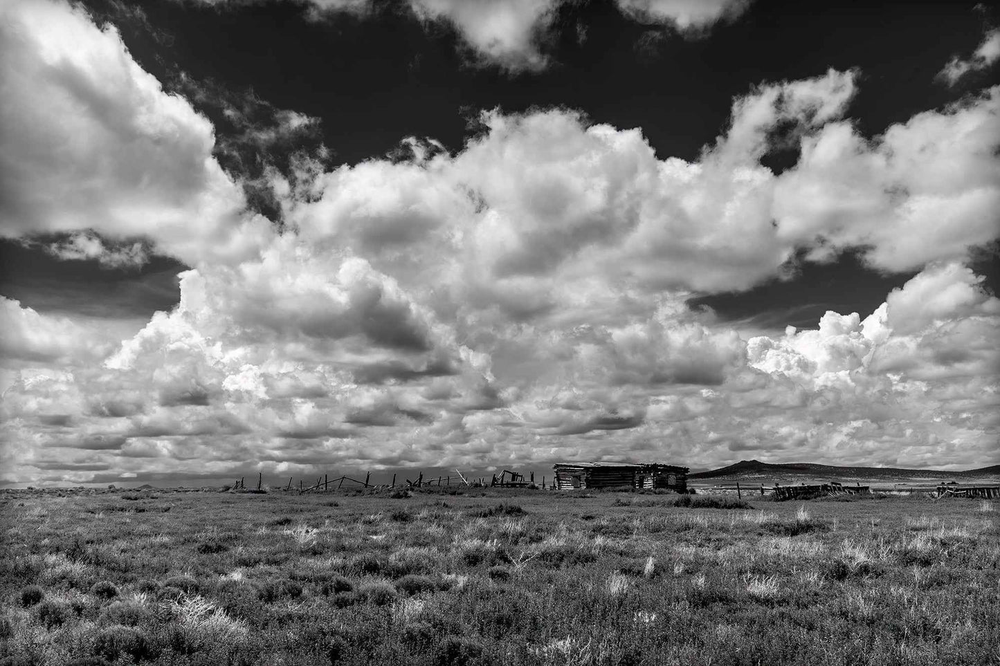 Abandoned Ranch — New Mexico black and white photograph of weathered structures beneath expansive cumulus clouds, a stark Western landscape defined by light and scale