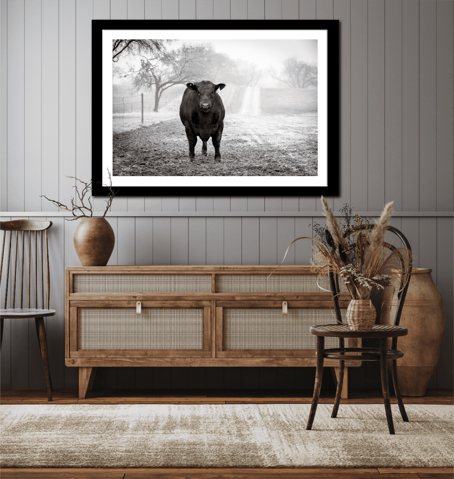 Framed black and white photo of a black Angus bull on a residence wall above a wooden cabinet.