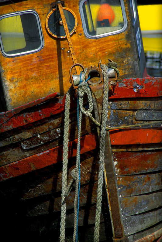 Fine art photograph of a weathered wooden boat bow with ropes and peeling paint at Port Askaig on the Isle of Islay, Scotland, emphasizing texture, color, and maritime atmosphere.
