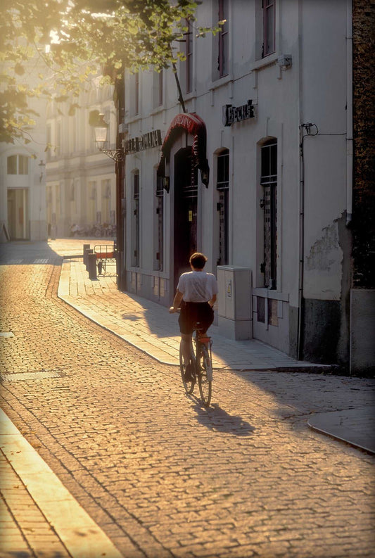 
Cyclist riding through golden light on a cobbled street in Bruges, Belgium, captured on Kodachrome film with long shadows.