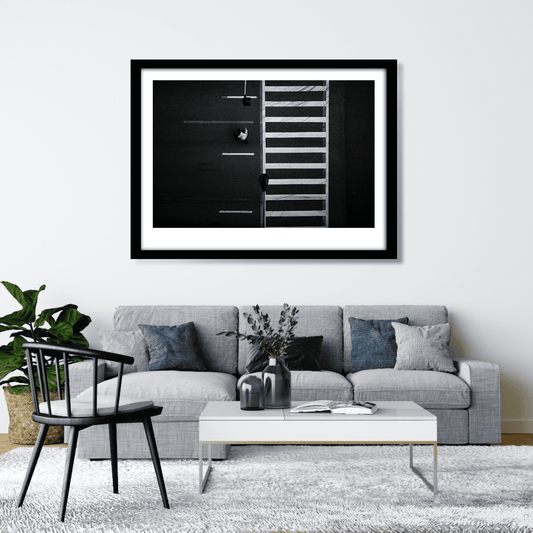 Framed overhead black and white photograph of Chicago crosswalk with pedestrian and graphic street pattern shown oin a clean neutral living room.