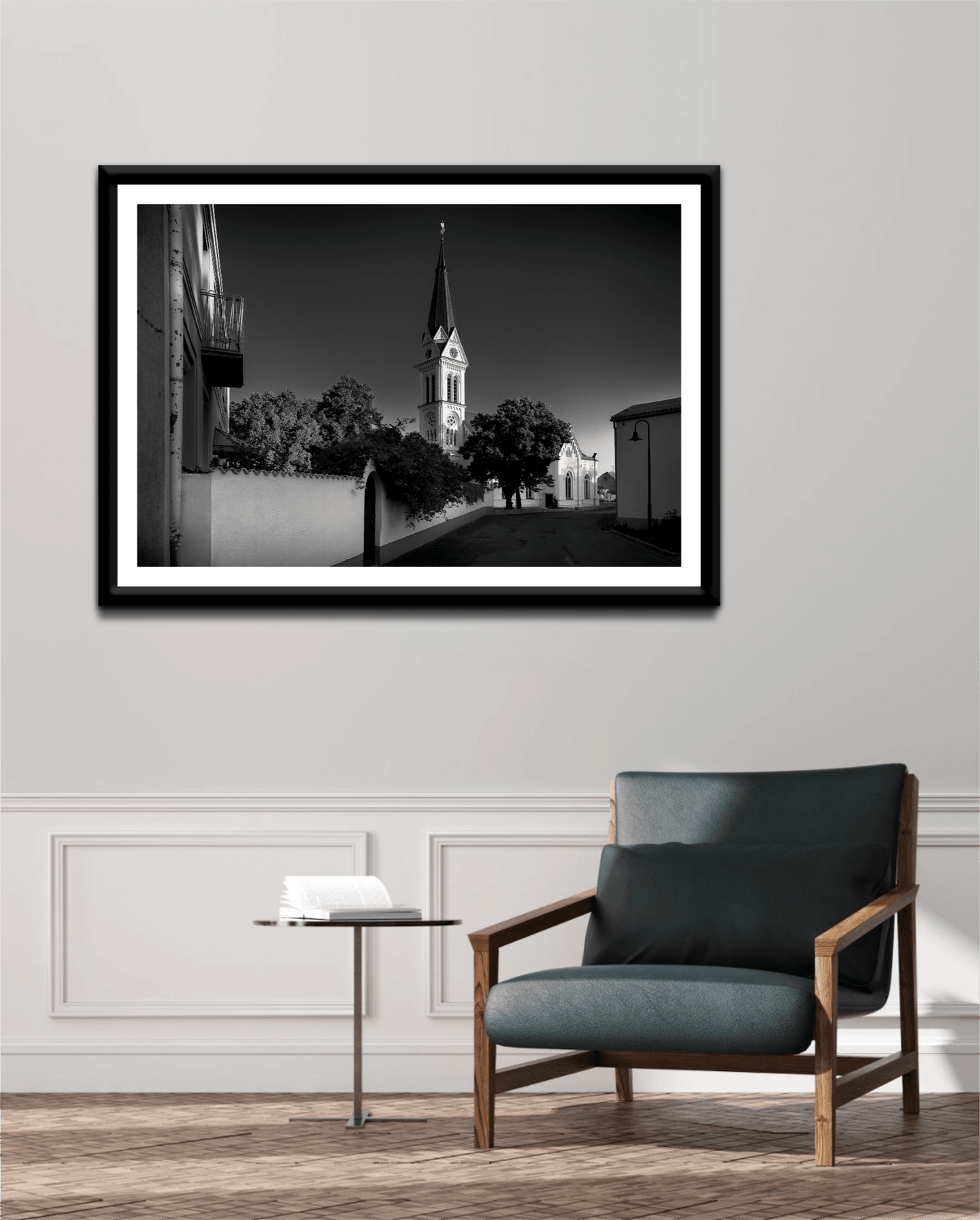 A framed print of the black and white image of an Autrian Church and Steeple in a room setting