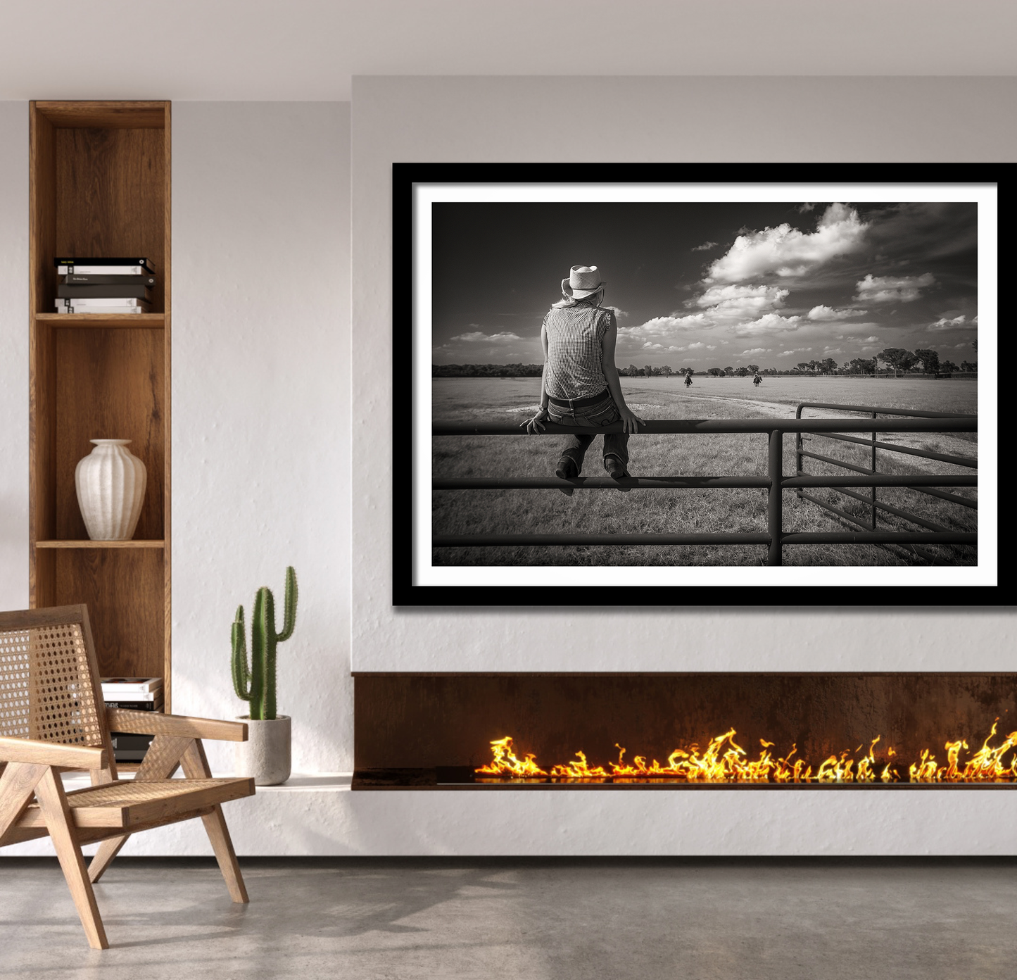 Framed black and white artwork of a woman sitting on a fence in a field, displayed in a modern living room.