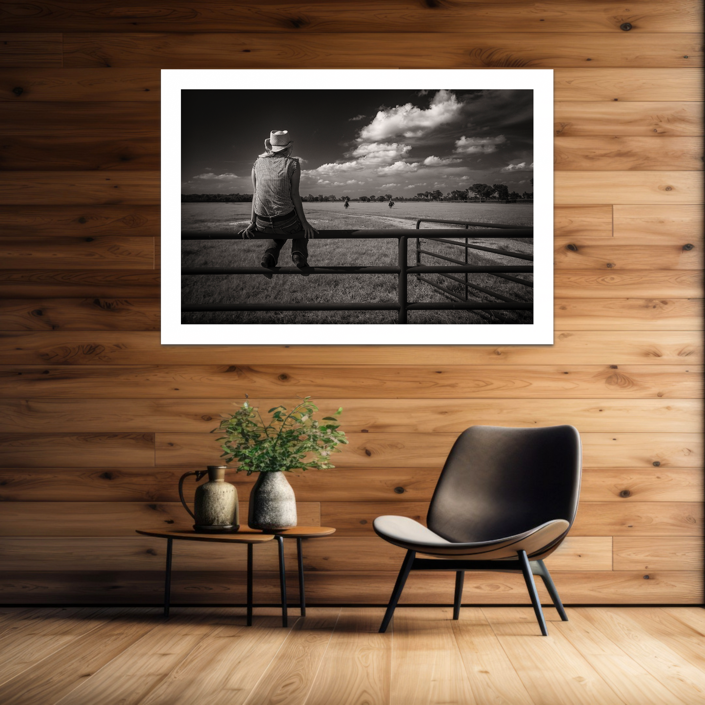 Framed black and white photo of ayoung woman sitting on a fence, displayed on a wooden wall above a chair and small table.