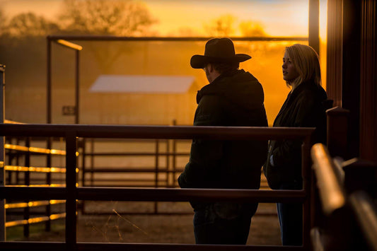 Two ranch hands silhouetted at sunrise in a Texas corral at 44 Farms, standing in quiet conversation in warm morning light.