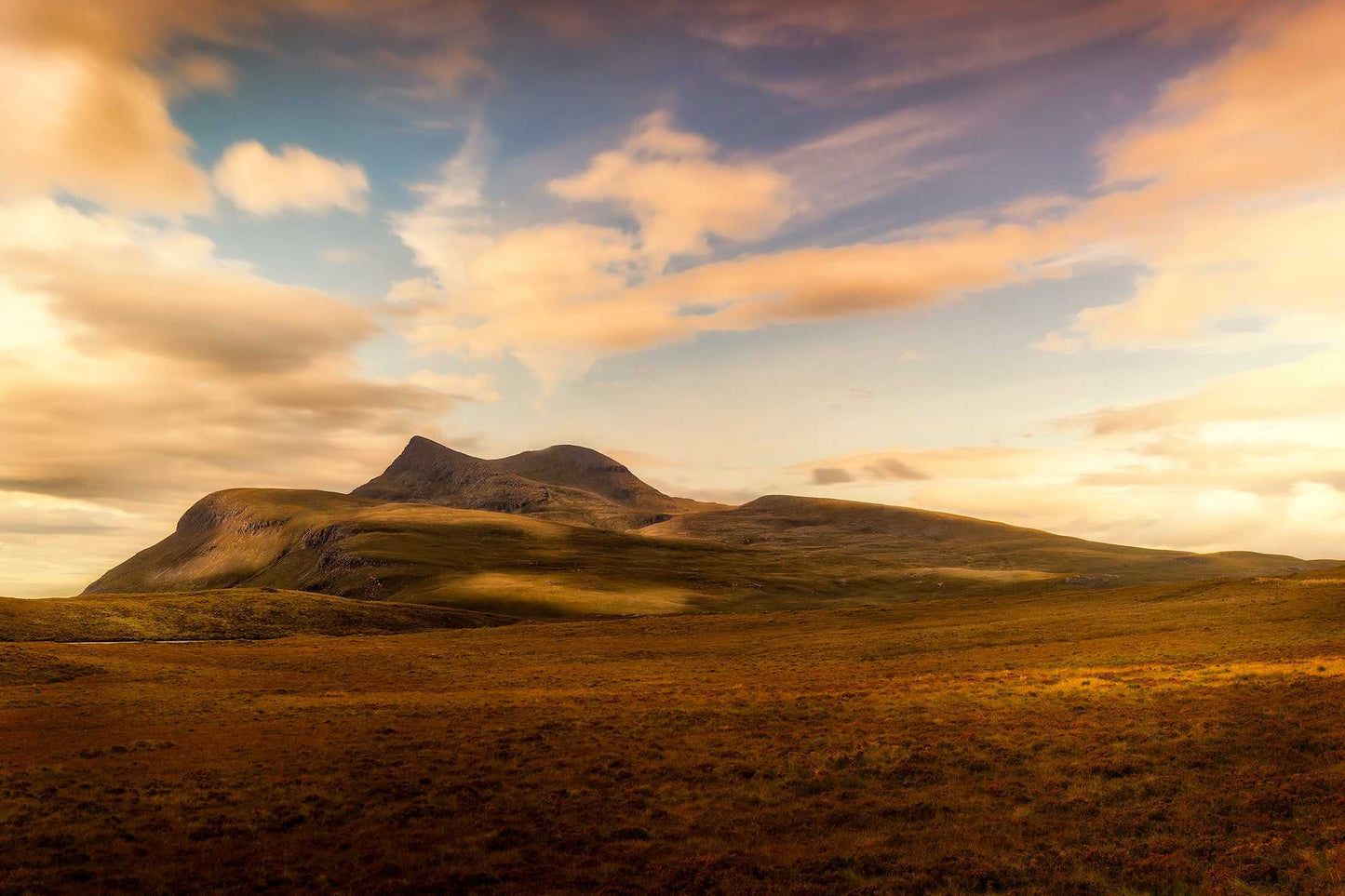 Fine art landscape photograph of Cùl Mòr in Inverpolly, Scottish Highlands, glowing in warm light above open moorland under dramatic clouds.