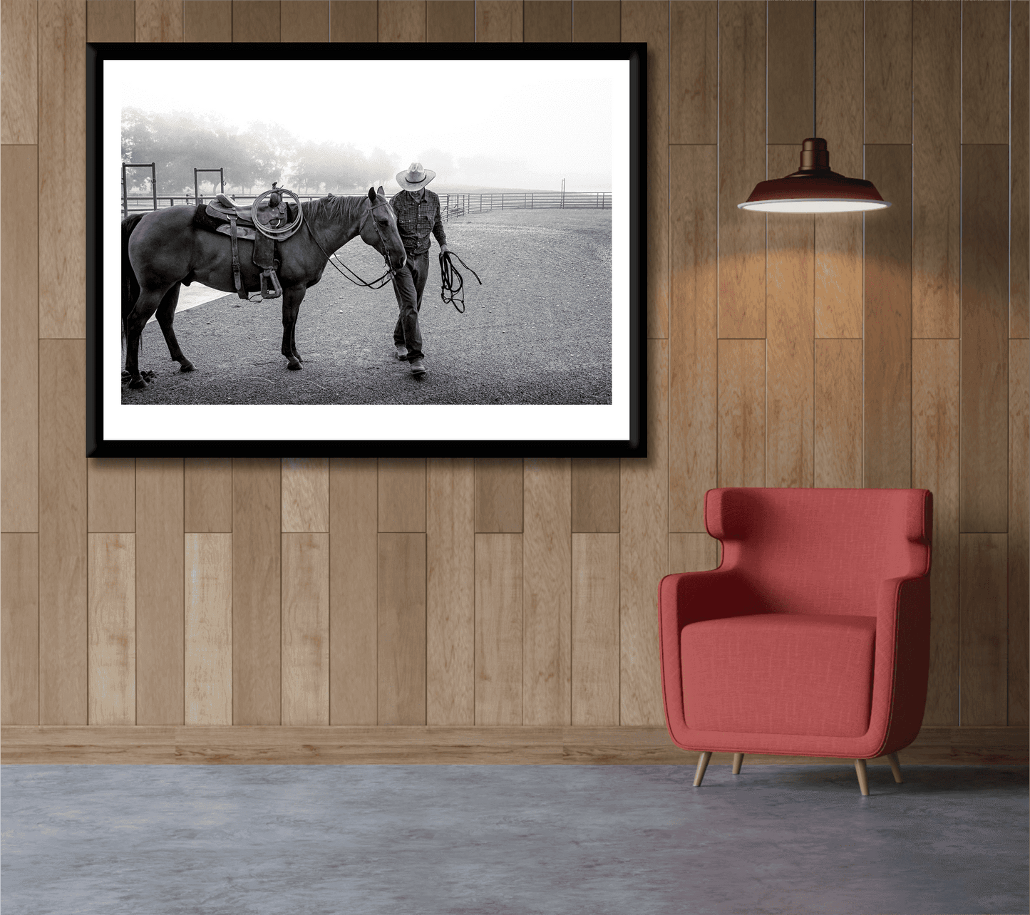 Morning Ride – Saddling Up in the Fog, Black and White Ranch Print by Michael Hart displayed on wood-paneled wall above red armchair. Limited edition Western art print featuring cowboy and horse in misty Texas ranch scene.