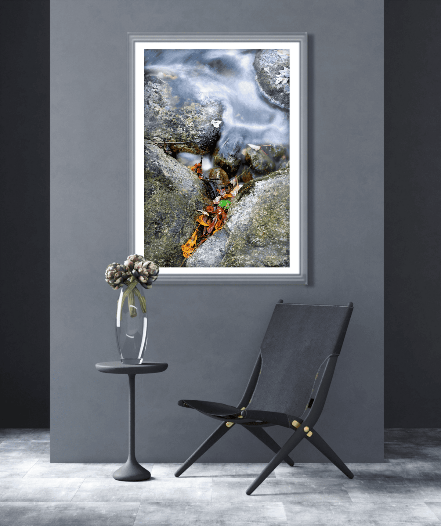 Fine art print First Frost featuring autumn leaves and rushing water, mounted in a sleek gray room with a black chair and floral accent table.