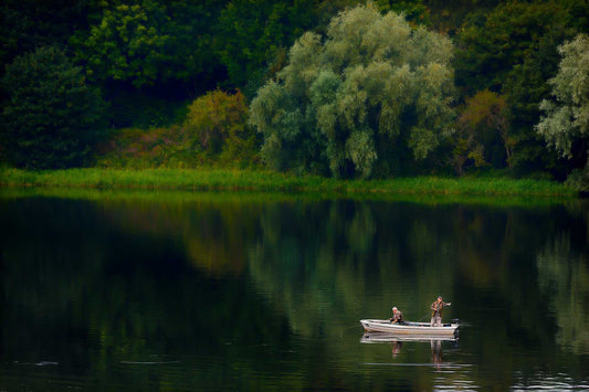 Fine art photograph of two fishermen in a small boat on Linlithgow Loch, Scotland, with calm water reflecting trees and soft natural light.