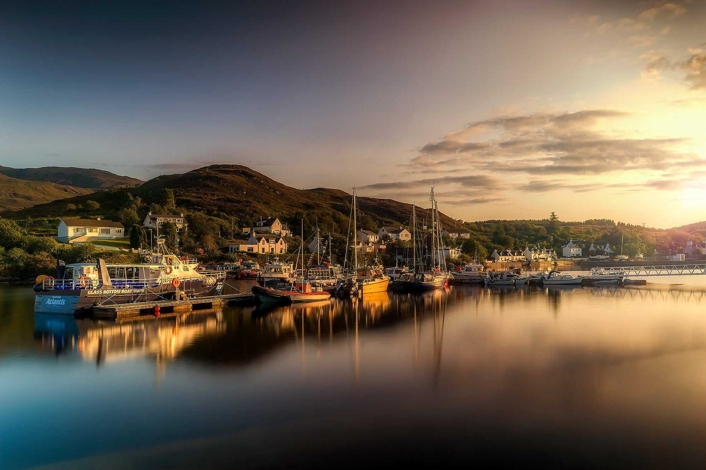 Fine art photograph of boats in Kyleakin Harbor on the Isle of Skye, Scotland, illuminated by warm evening light with reflections in still water.