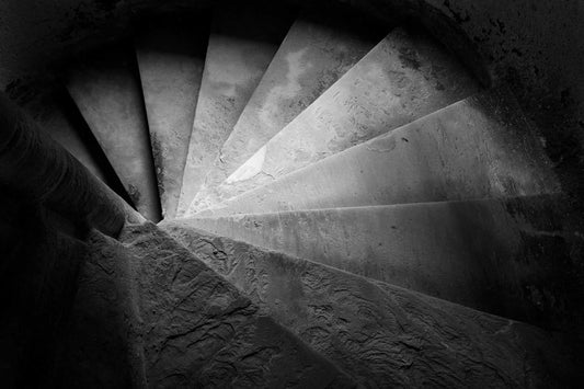 Black and white photograph of a spiral stone staircase in Linlithgow Palace, Scotland, emphasizing sweeping curves, shadow, and textured surfaces