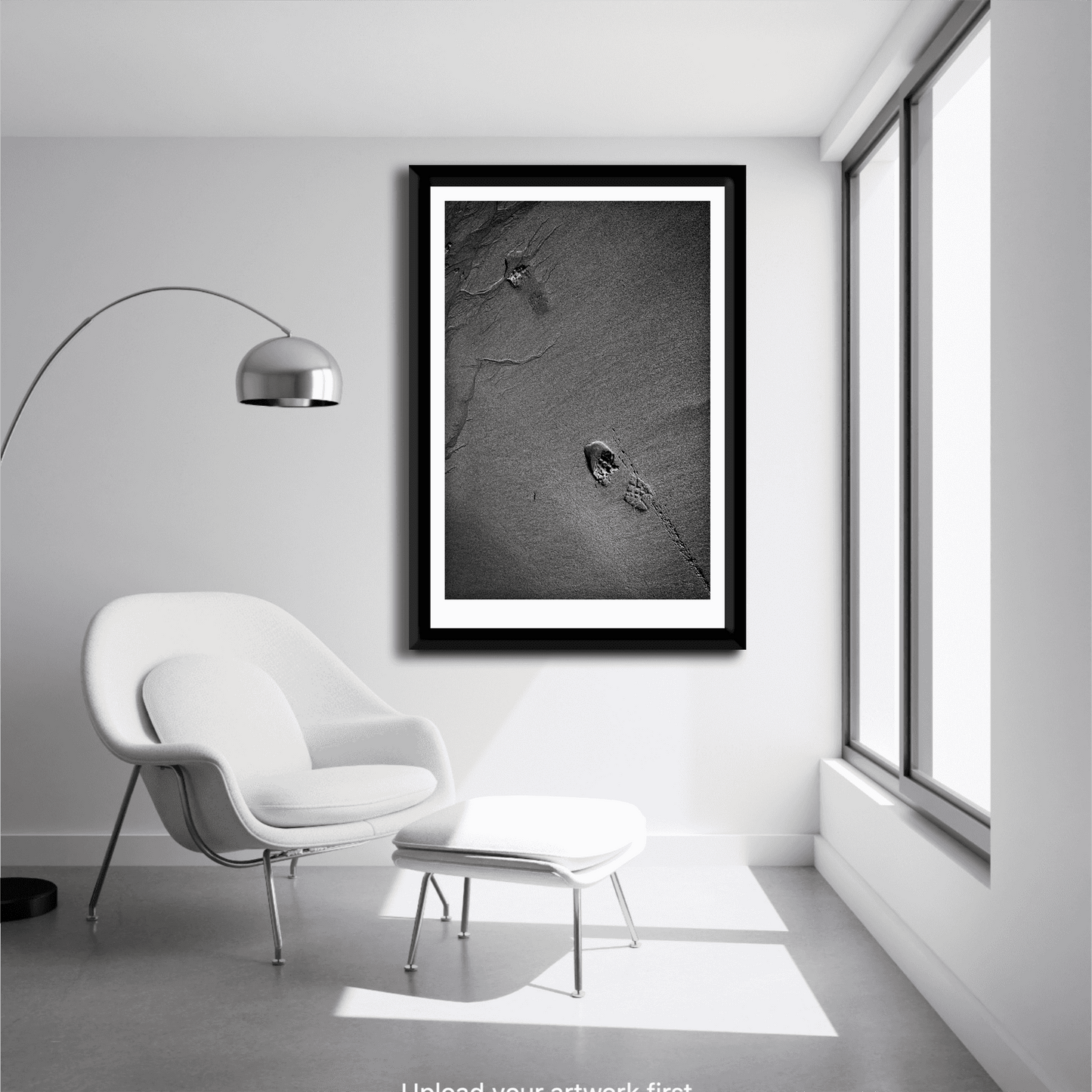 Minimalist room with lounge chair featuring framed Traces #1 – black and white sand and footprint fine art print in vertical composition.